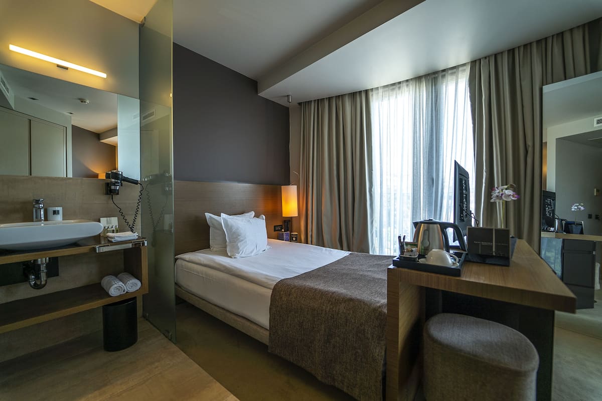 A hotel room with a bed, bedside table, lamp, and a desk with a chair.