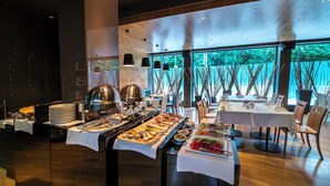 A buffet setup with various food items and a dining area with tables and chairs. - Hotel mOdus (Varna)