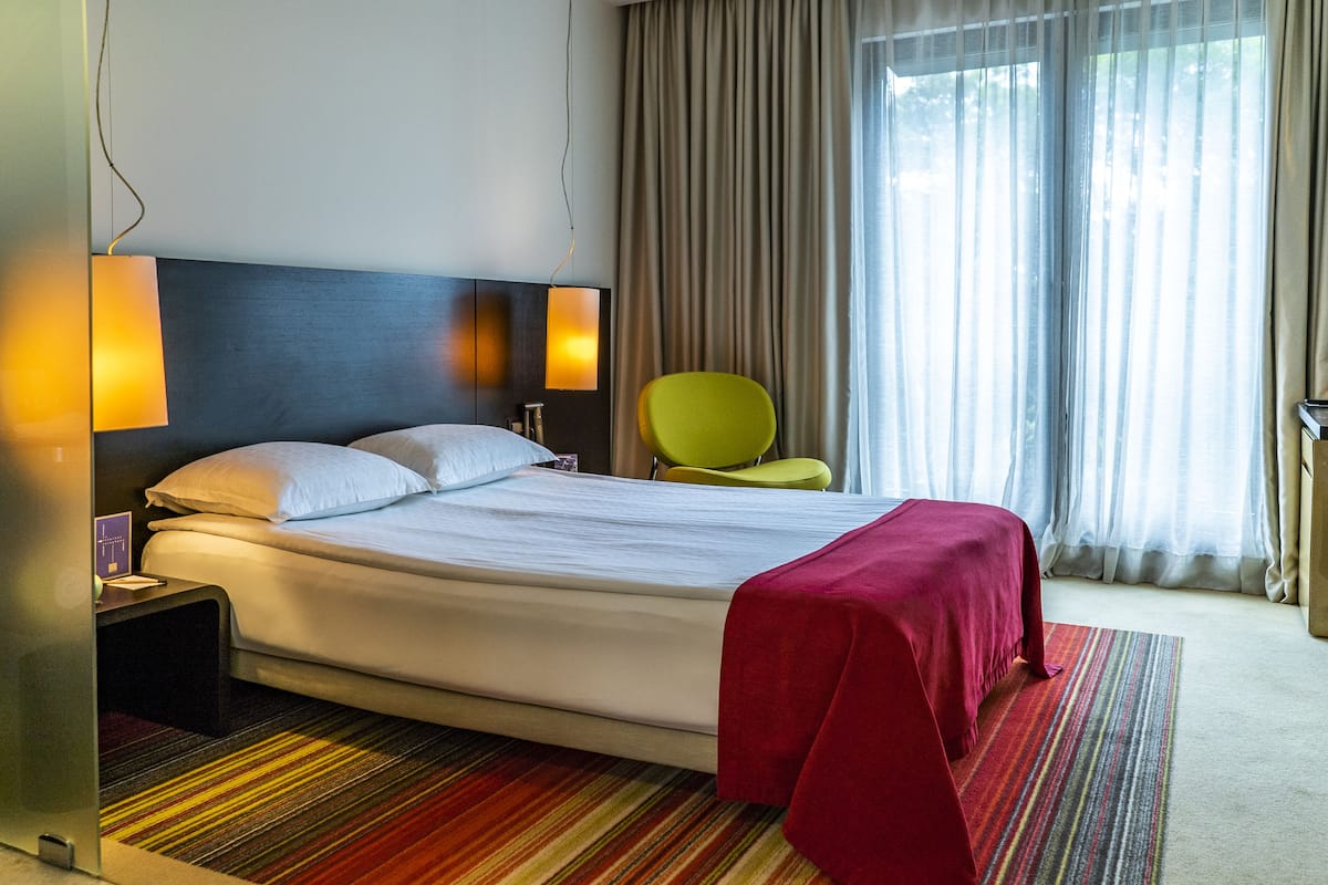 A hotel room with a large bed, two bedside lamps, a chair, and a window with curtains.