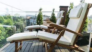A wooden deck with two lounge chairs and a small table, overlooking a cityscape with trees and buildings. - Hotel mOdus (Varna)