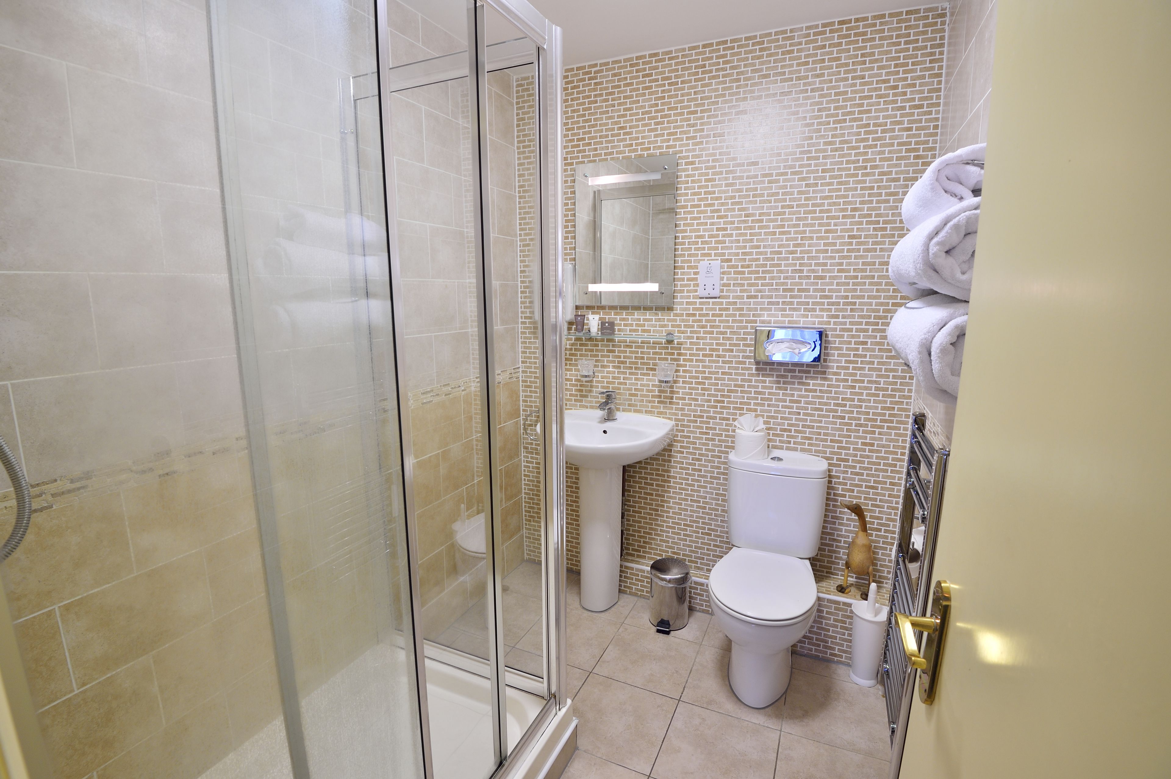 Une salle de bain avec une douche à parois de verre, un lavabo blanc, des toilettes et un porte-serviettes avec des serviettes.