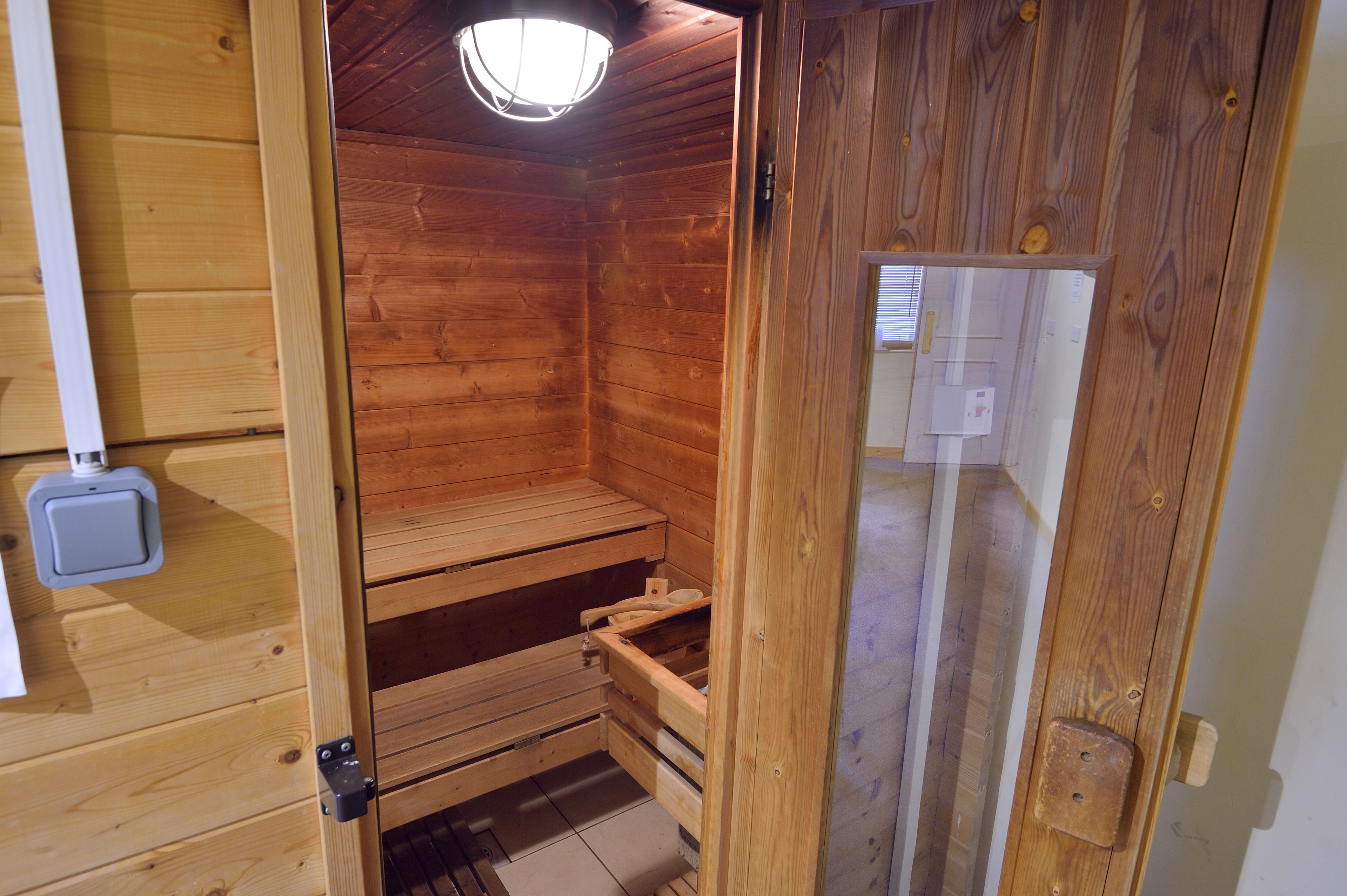A wooden sauna with a bench, a light fixture, and a door with a handle.