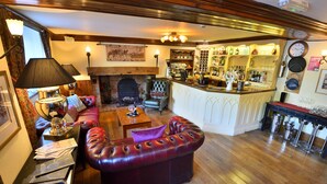A cozy bar area with a fireplace, leather seating, and a well-stocked bar. - Angmering Manor (Littlehampton)
