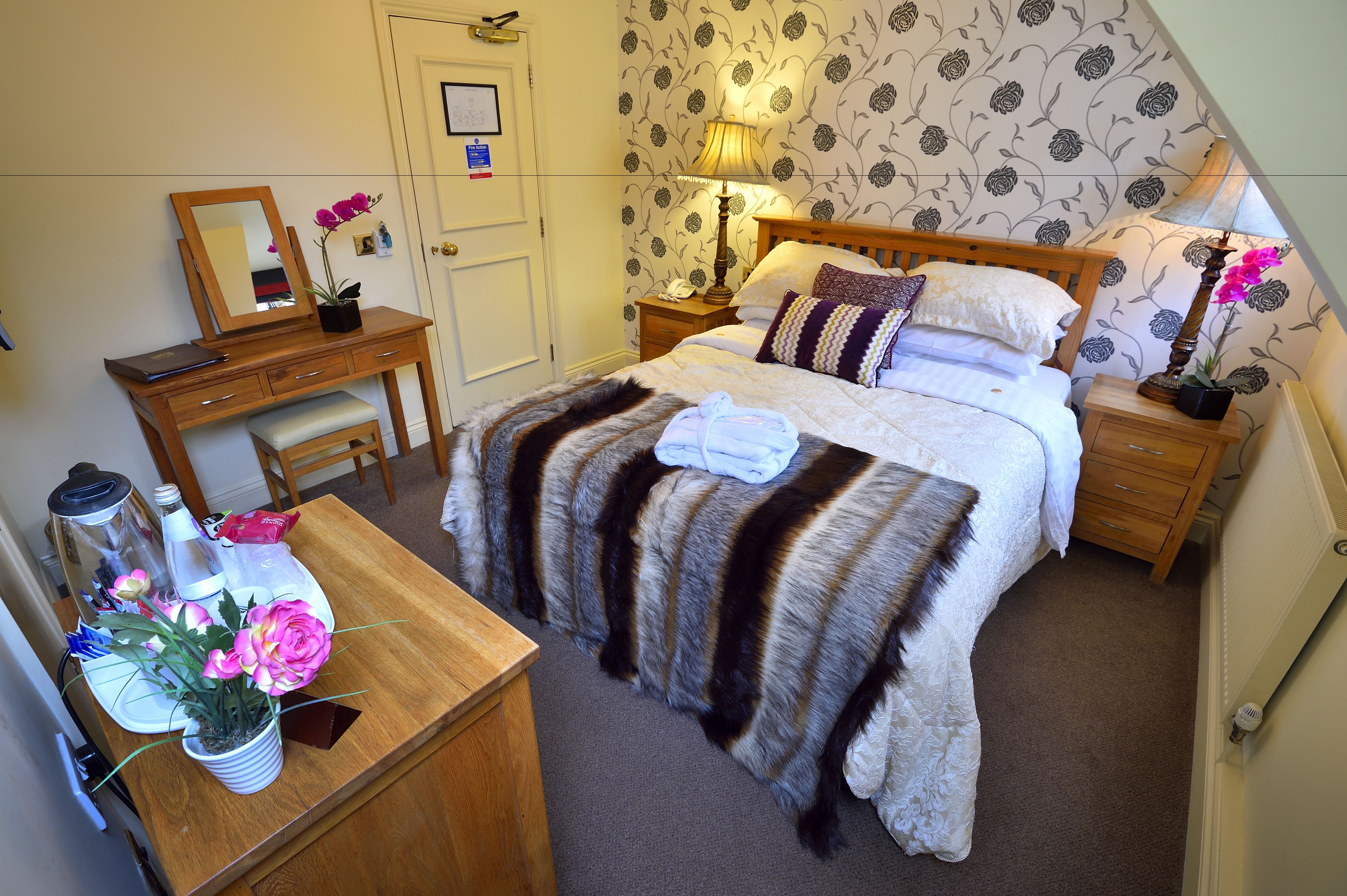 A neatly arranged bedroom with a bed, bedside tables, a desk, and a chair.