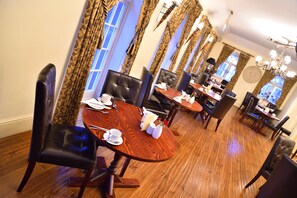 A dining area with a round wooden table, black leather chairs, and a chandelier.