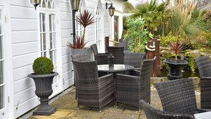 A patio with wicker furniture, a round table, and potted plants. - Angmering Manor (Littlehampton)