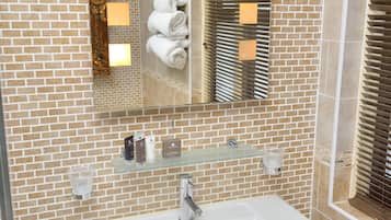 Un baño con lavamanos blanco, repisa de vidrio con artículos de tocador y espejo con toallero.