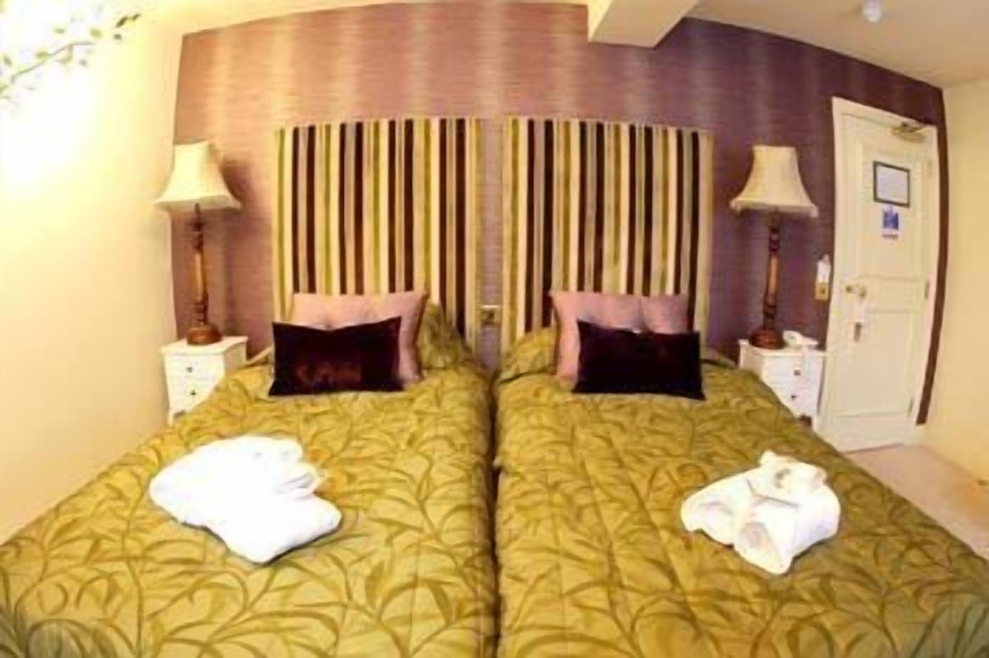 A double room with two beds, each with a pillow and a lamp on a bedside table.