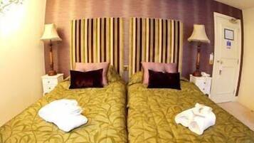 A double room with two beds, each with a pillow and a lamp on a bedside table.