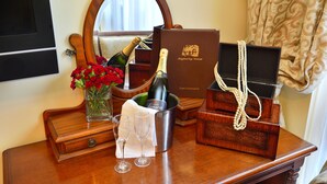 A wooden dresser with a mirror, a bottle of champagne, a vase of red roses, and a jewelry box. - Angmering Manor (Littlehampton)