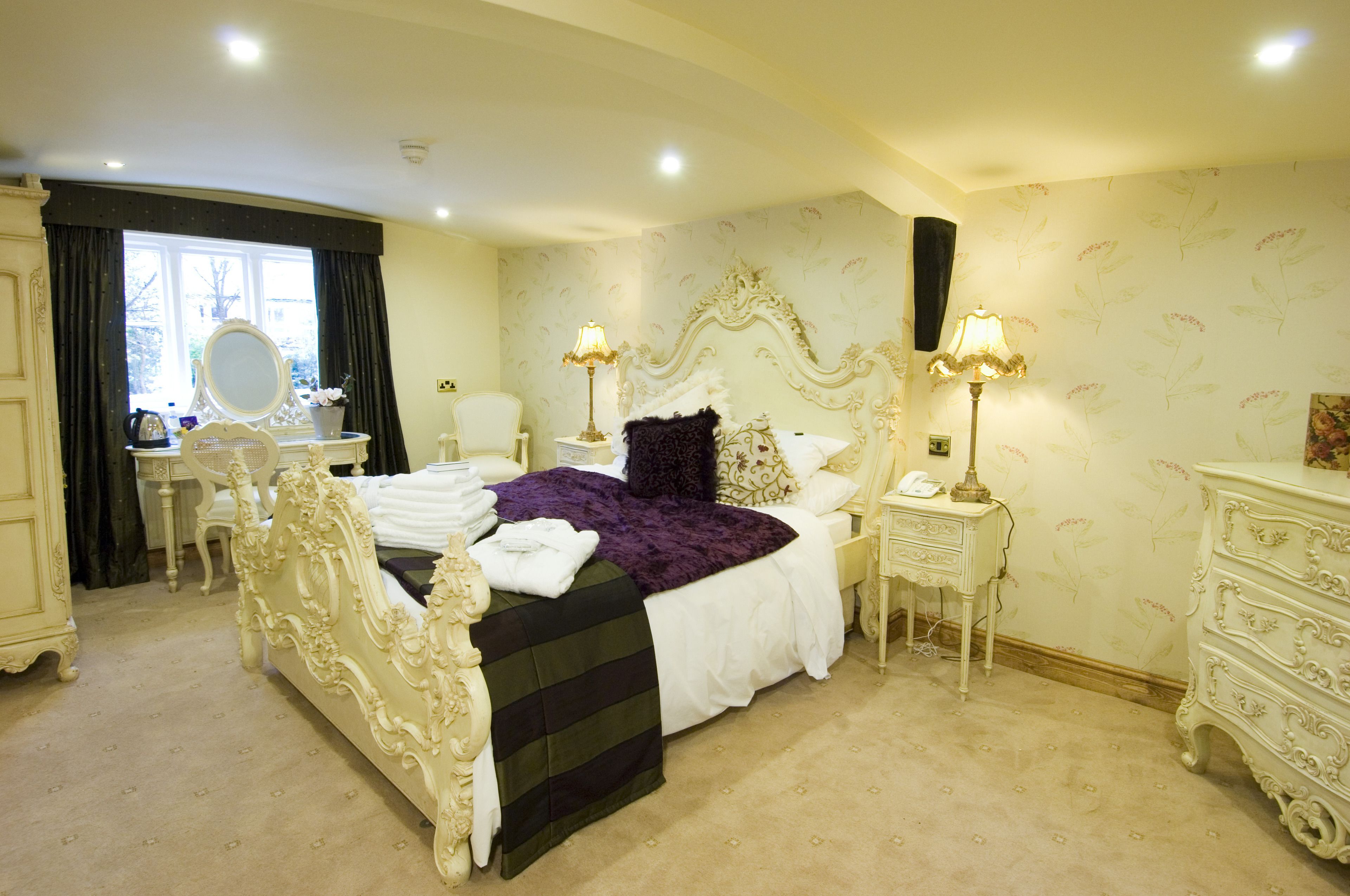 Un dormitorio con una cama grande y ornamentada, un tocador con espejo, un aparador y una lámpara.
