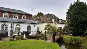 A traditional house with a pond, a wooden bridge, and a well-maintained garden. - Angmering Manor (Littlehampton)