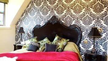 Un dormitorio con papel tapiz estampado, cabecero oscuro y colcha roja.