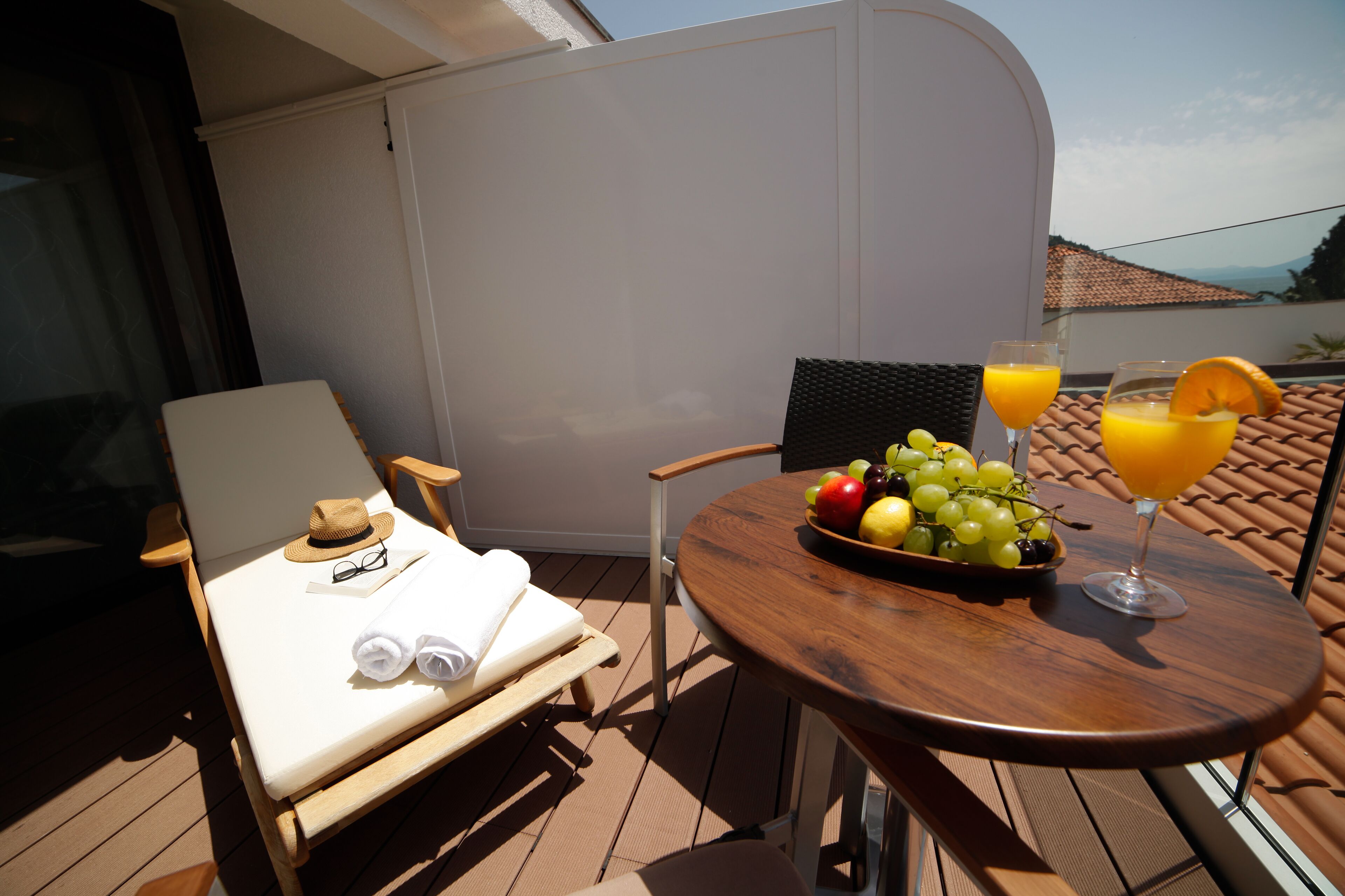 Un pontile illuminato dal sole con una poltrona da relax, un tavolino con frutta e bevande, e vista sul mare.