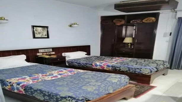 A hotel room with two beds, a wooden headboard, a nightstand, a lamp, and a wardrobe.