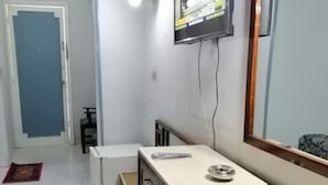 A small, clean room with a desk, a television mounted on the wall, and a mirror.