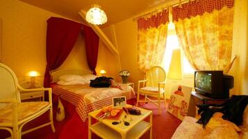 Una habitación acogedora con cama, una silla, una mesita con frutas, televisión y cortinas.