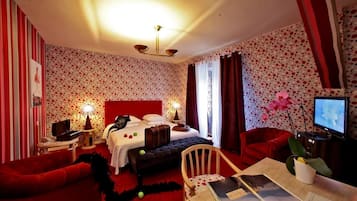 A hotel room with a bed, a desk with a chair, a TV, and a red sofa.