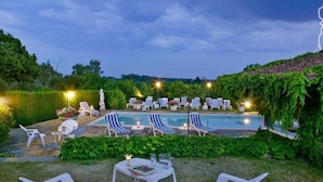 Zona de piscina con sillones de descanso y una mesa, rodeada de follaje y senderos de piedra.
