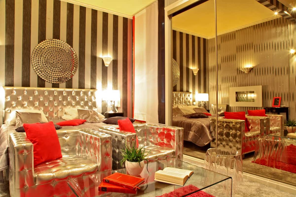 Une chambre d’hôtel moderne avec un mur à rayures, une tête de lit capitonnée, une table basse en verre et un mur miroir.