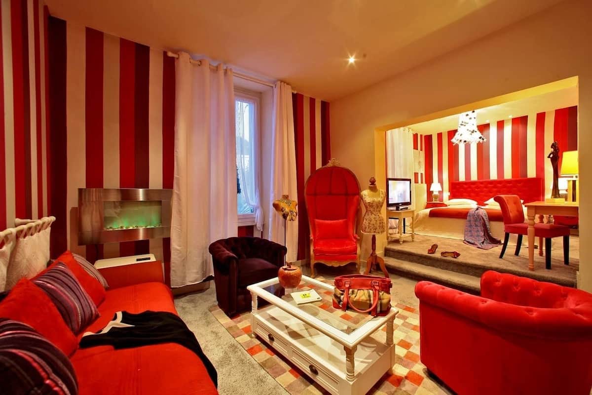 Un salon avec un canapé rouge, un téléviseur et une grande fenêtre avec des rideaux.