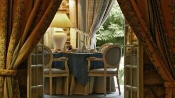 Un comedor con una mesa dispuesta para dos personas, rodeado de cortinas y una lámpara.