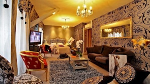 Un salón luminoso con televisor grande, sofá, sillón rojo y alfombra estampada.