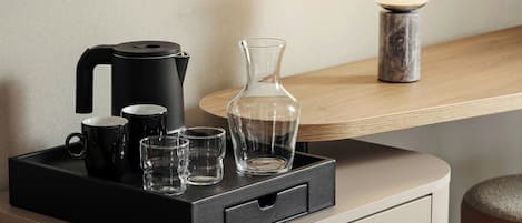 A black tray with a coffee maker, two black mugs, and three clear glasses on a wooden table.