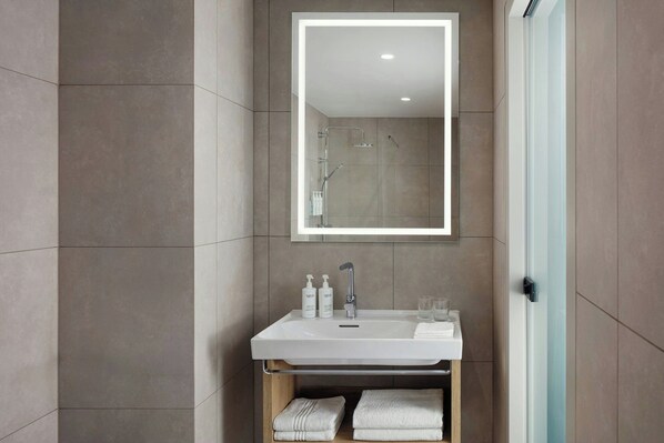 A modern bathroom with a white sink, two bottles of shampoo, a mirror, and two towels.