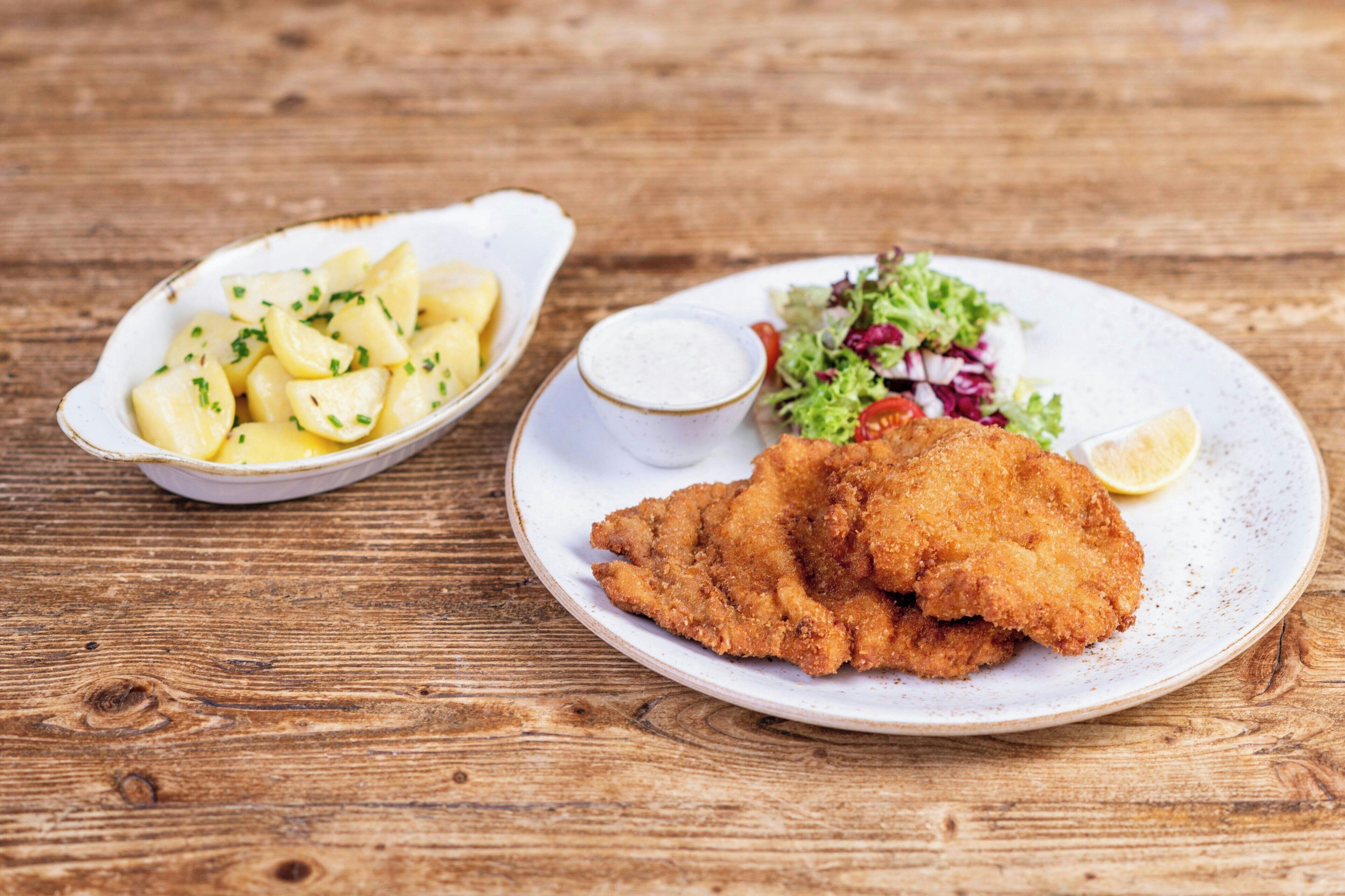 A plate of breaded and fried food with a side of potato salad and a small bowl of sauce.