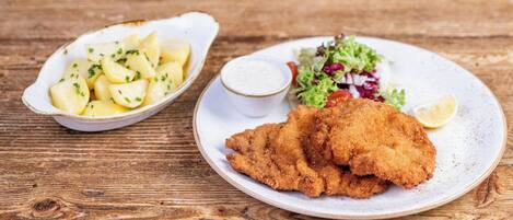 A plate of breaded and fried food with a side of potato salad and a small bowl of sauce.