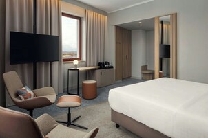 Una habitación de hotel moderna con una cama grande, un escritorio con lámpara, una silla, un televisor y un armario.