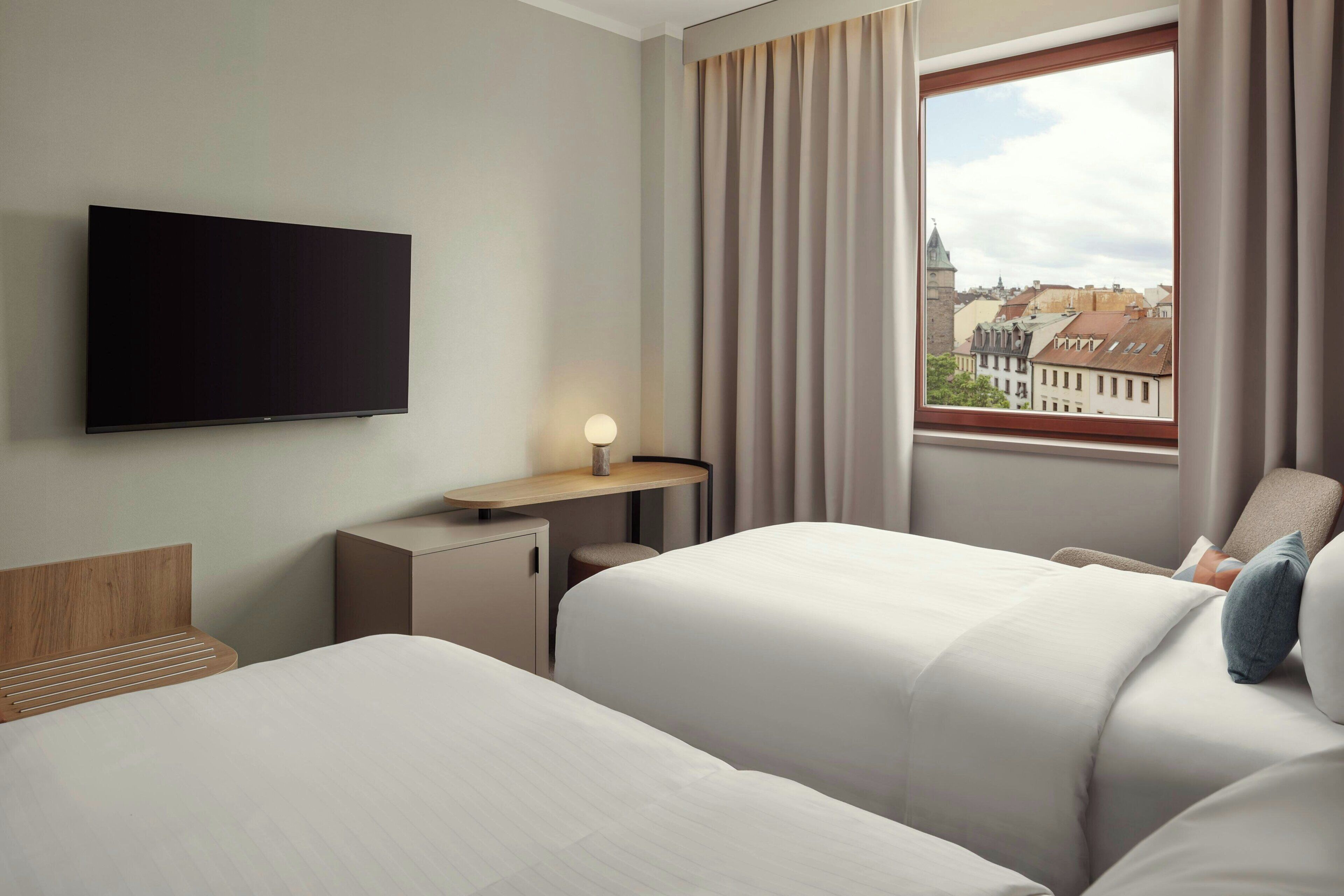 Habitación de hotel con cama, escritorio, televisor y ventana con vista a la ciudad.