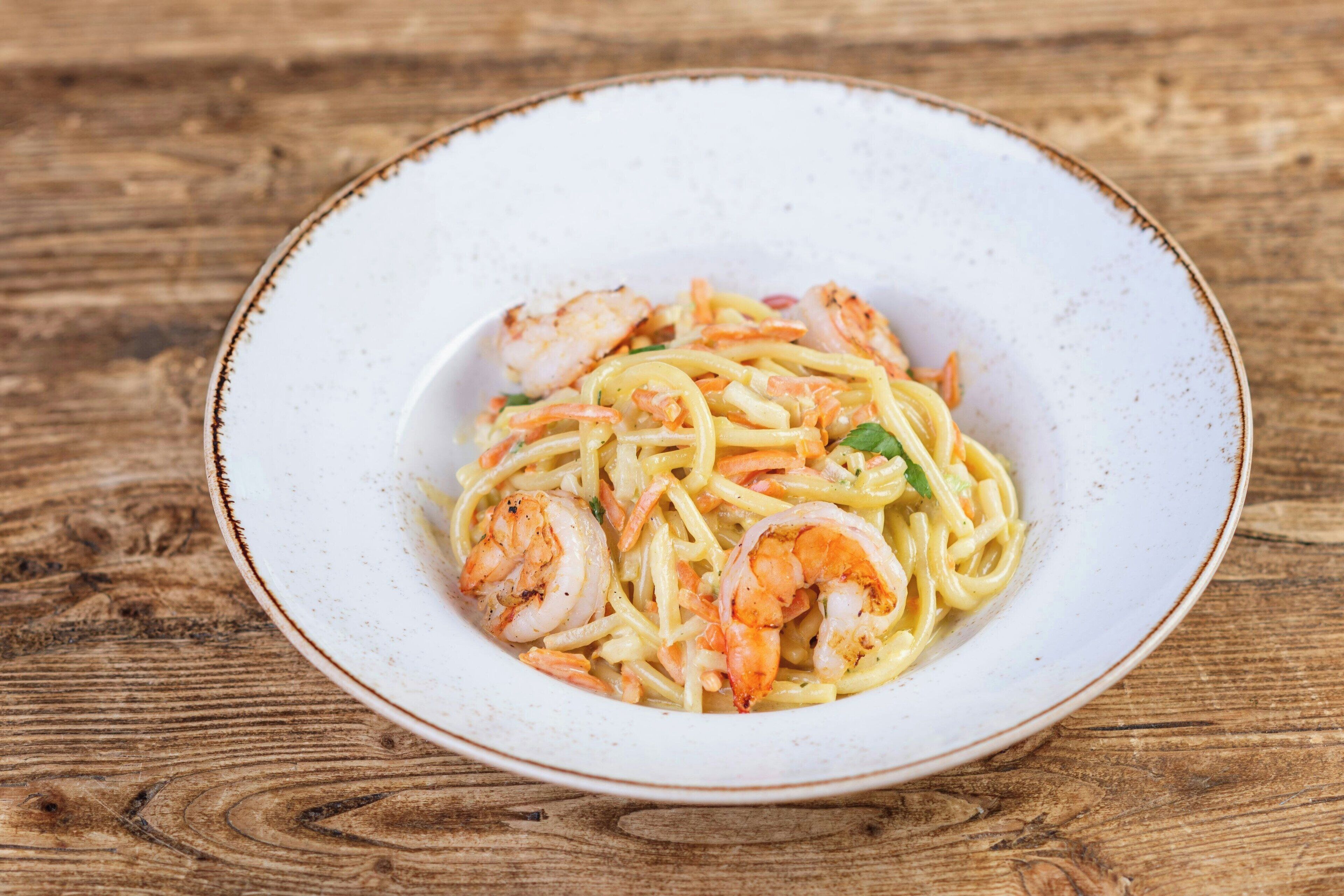 Een schaal pasta met garnalen op een houten tafel.