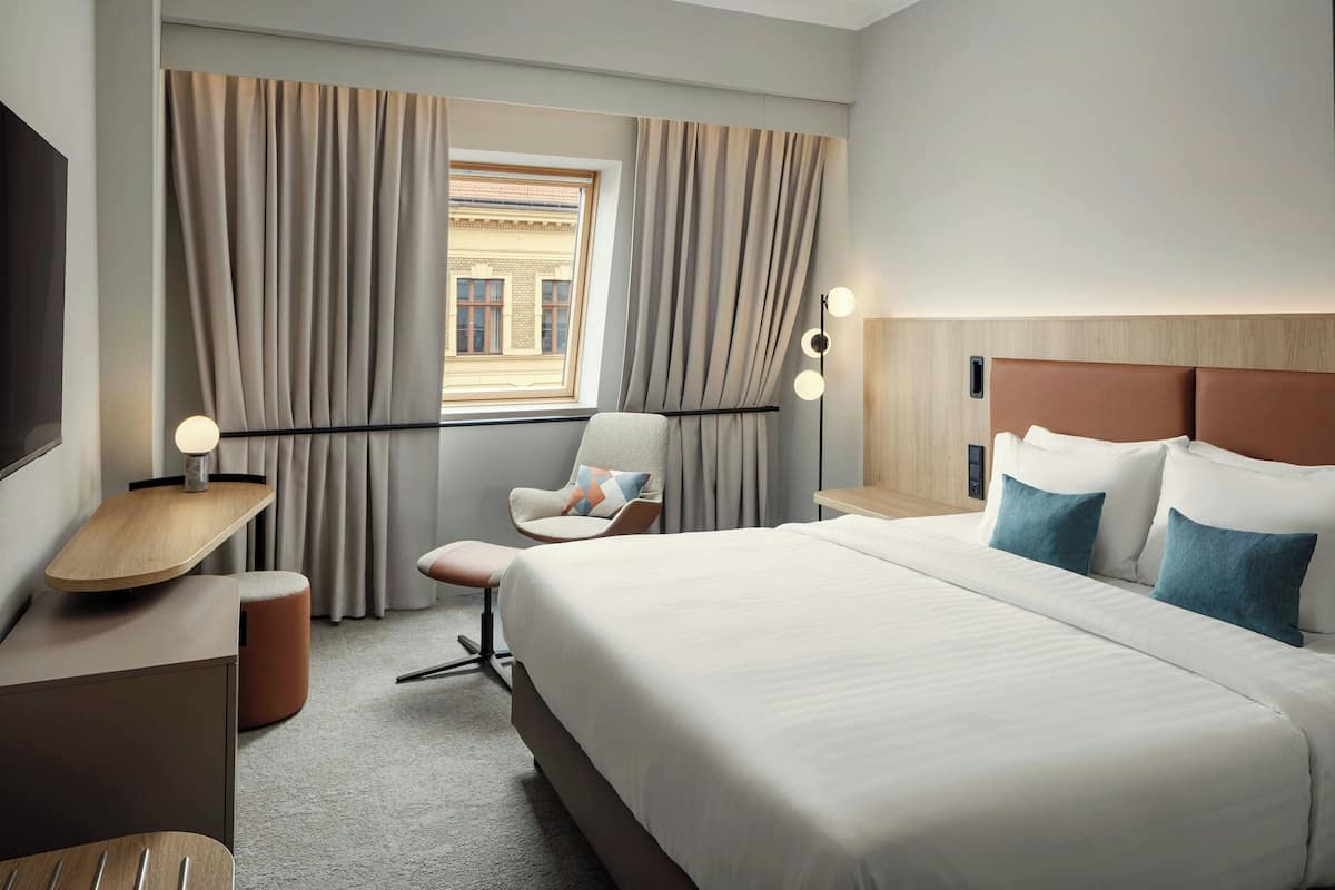 Habitación de hotel moderna con una cama grande, un escritorio, una silla y vistas a un edificio a través del ventanal.