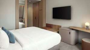 Una habitación de hotel moderna con una cama grande, un televisor montado en la pared, una pequeña zona de estar y un mueble de almacenamiento compacto.