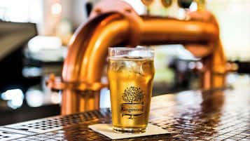 A glass of beer with a tree logo on a coaster, placed on a table with a metal grid pattern.