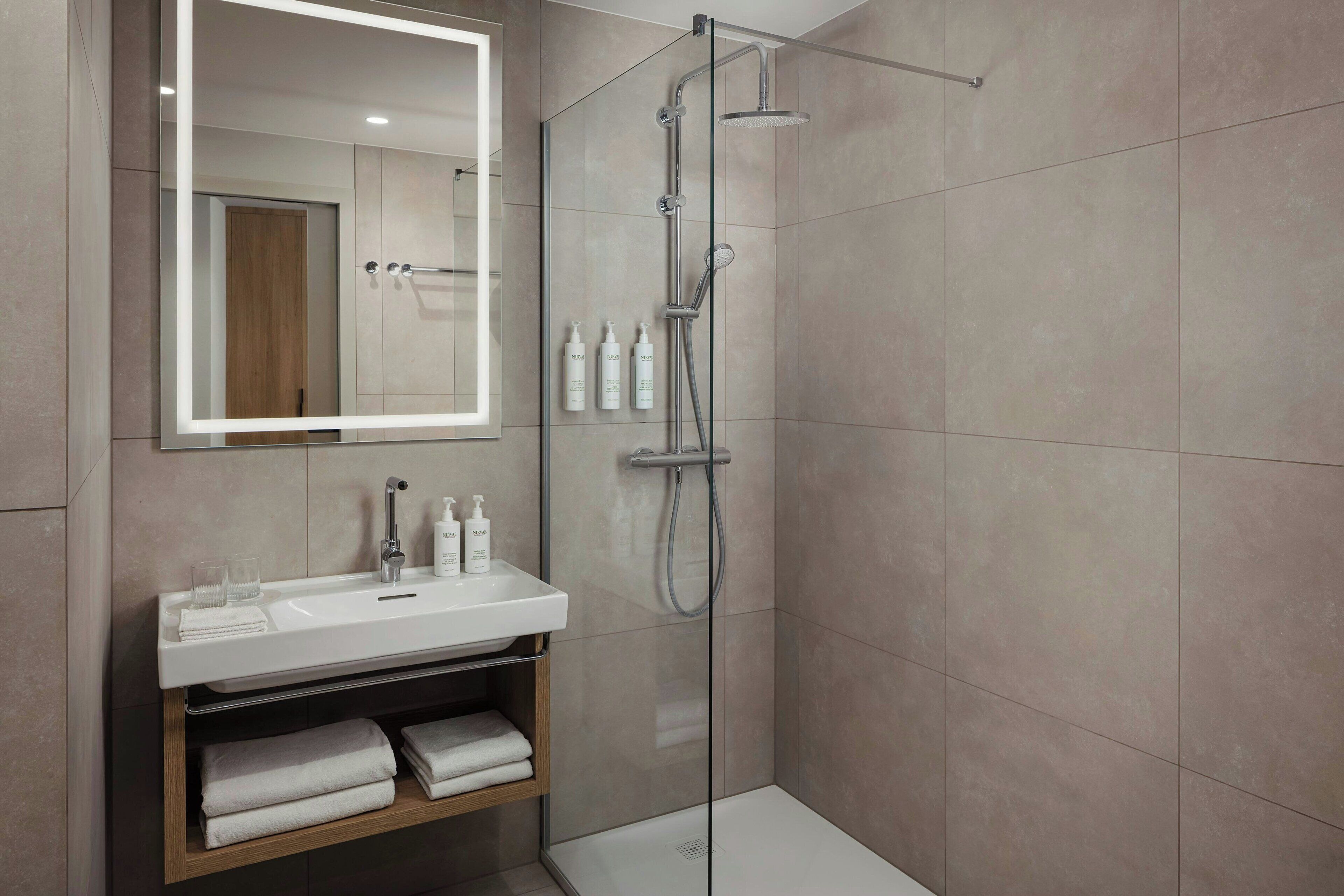 Un baño moderno con ducha de vidrio, lavamanos blanco y espejo sobre él.