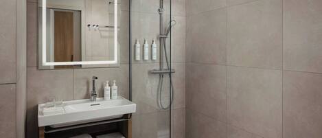 Un baño moderno con ducha de vidrio, lavamanos blanco y espejo sobre él.