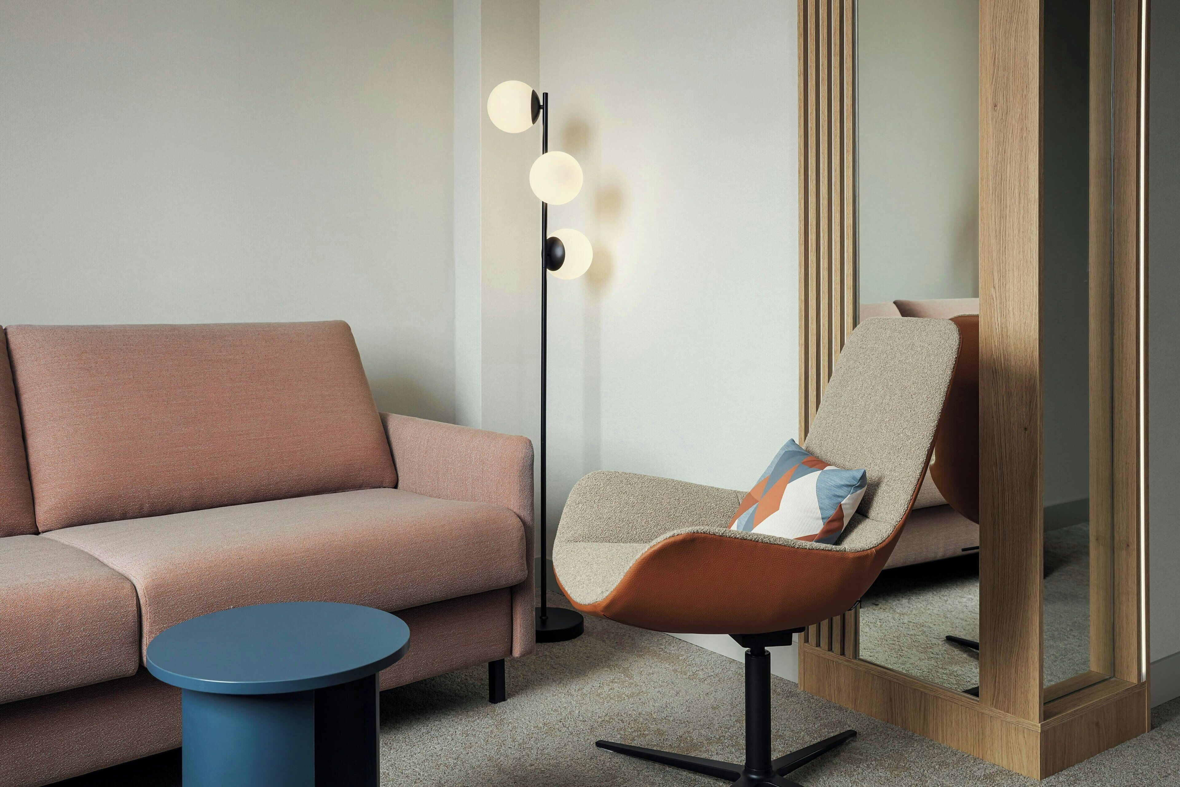 A modern living room with a sofa, a chair, a small round table, and a floor lamp with three lights.