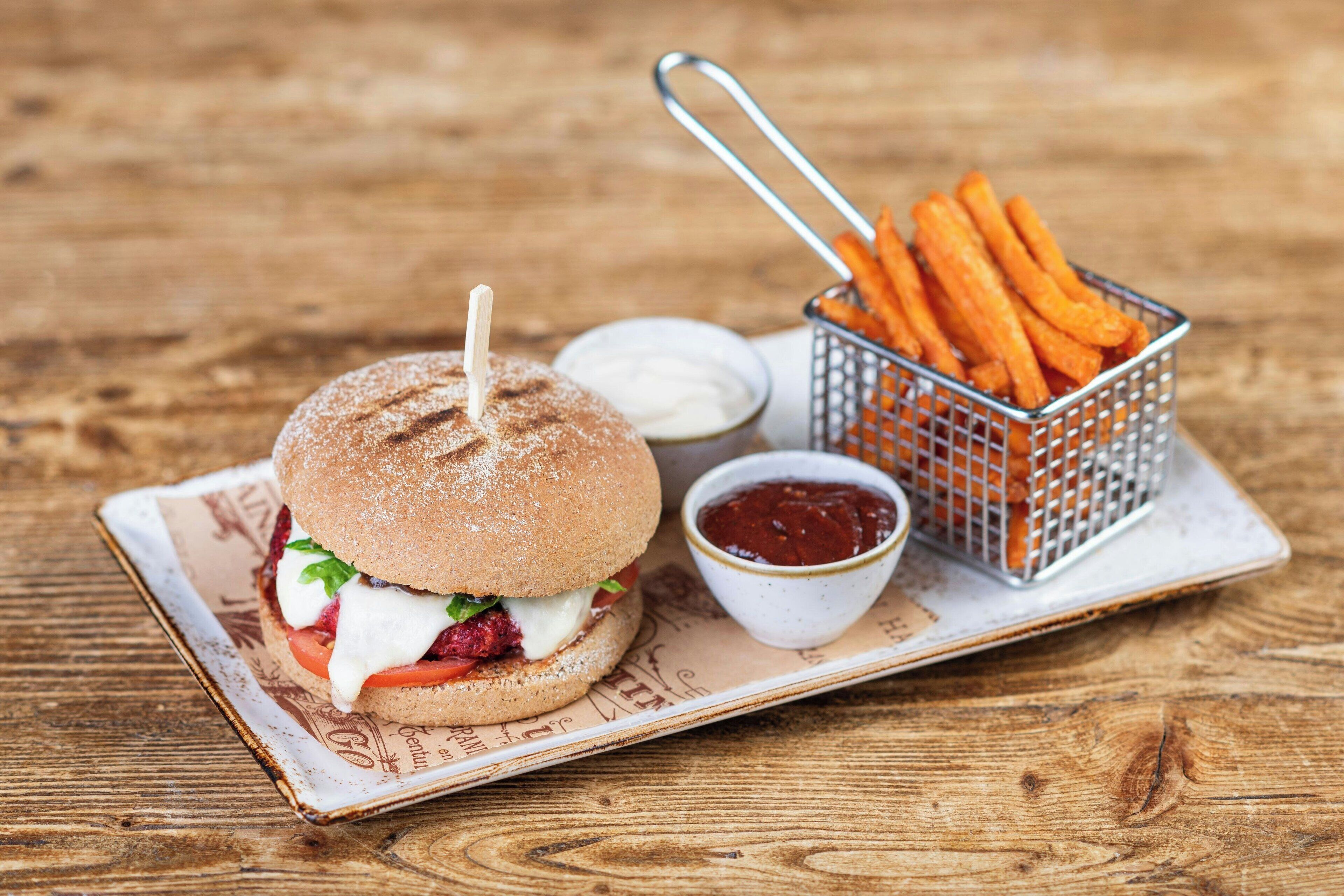 Una hamburguesa amb patates i ketchup damunt un taulell de fusta.