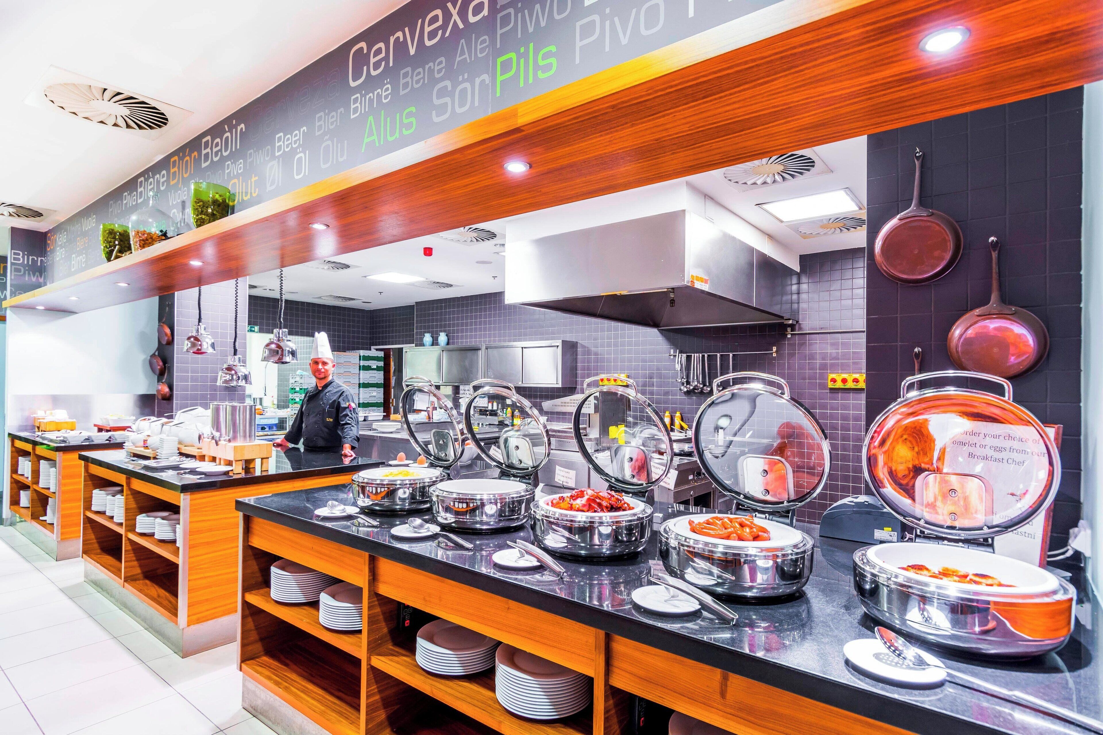 A buffet area with multiple food stations, a chef, and a modern kitchen in the background.