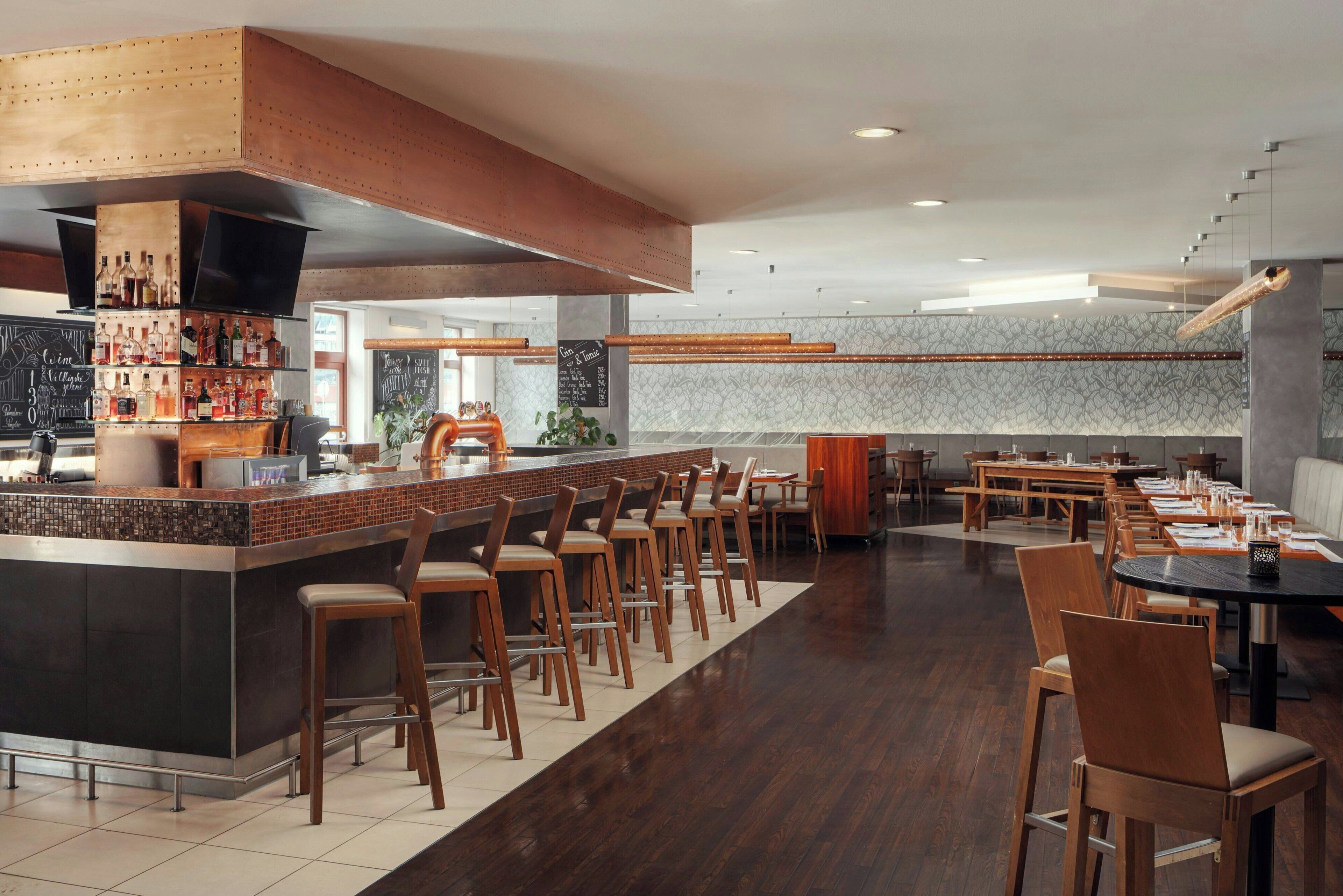 A modern bar area with a long counter, multiple stools, and a variety of bottles.