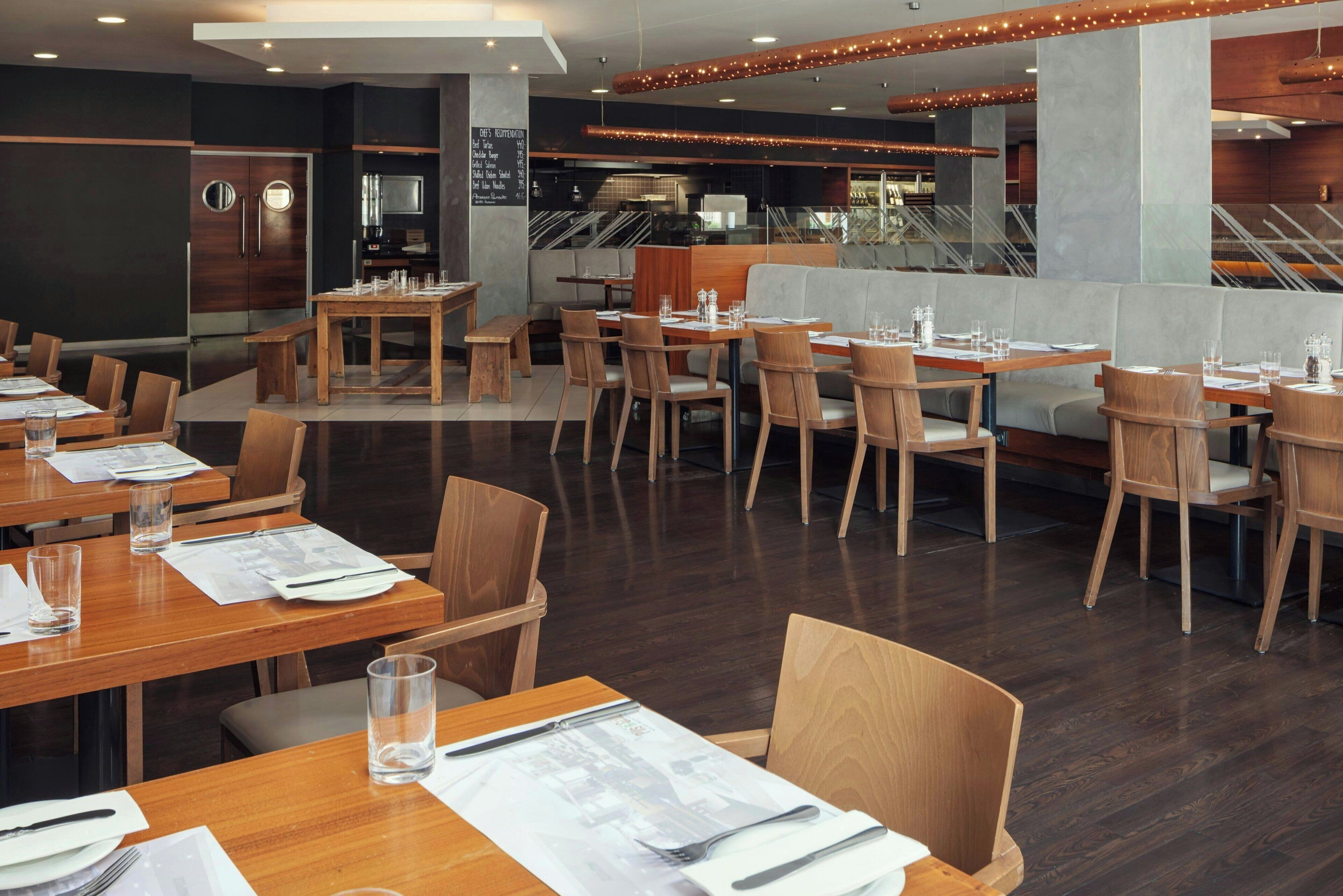 Een restaurant met houten tafels en stoelen, een menubord en een trap op de achtergrond.