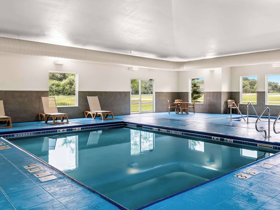 An indoor swimming pool with clear lane markings, wooden lounge chairs, and large windows offering views of the outdoors.