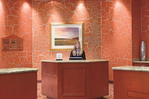 Een receptiebalie met erboven een lijst met een landschapsafbeelding, een bord met informatie over het hotel, en een vaas aan de rechterkant.