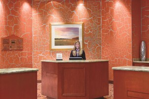 A reception desk with a framed landscape painting above it, a signboard with hotel information, and a vase on the right.