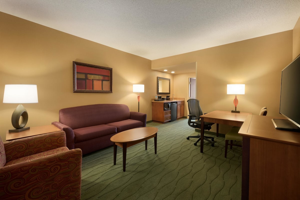 Ein Hotelzimmer mit einer Couch, einem Sessel, einem Schreibtisch und einem Fernseher.