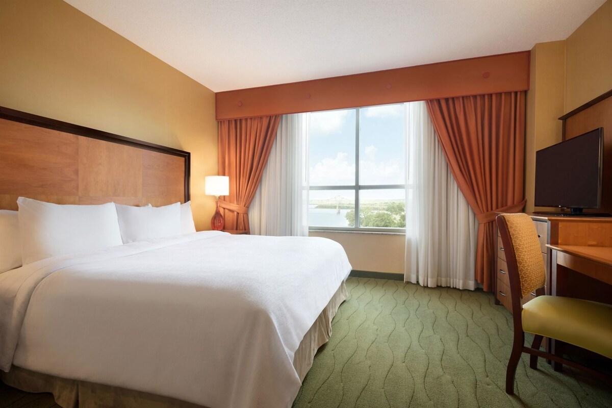 Une chambre d’hôtel avec un grand lit, un bureau avec une chaise, une télévision et une fenêtre avec des rideaux.