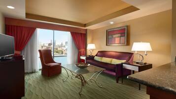 A hotel room with a large window, a sofa, a chair, a TV, and two lamps.